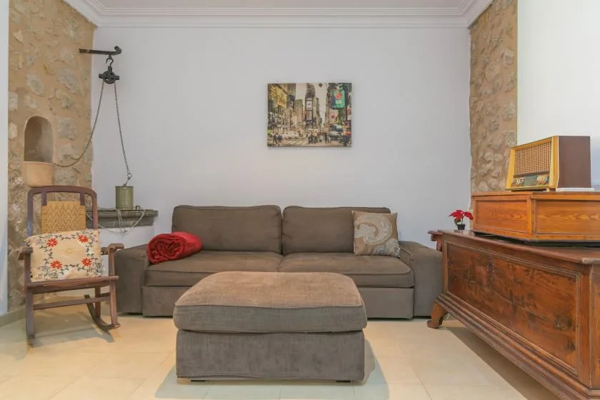 A living room with a sofa, an upholstered footstool, and wooden furnishings.