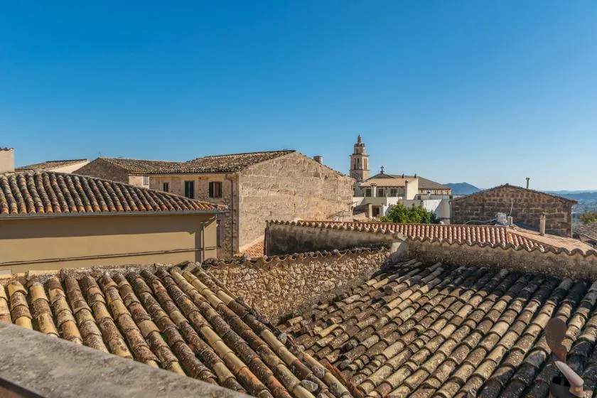 Rooftops of a town with a bell tower beneath a clear blue sky.