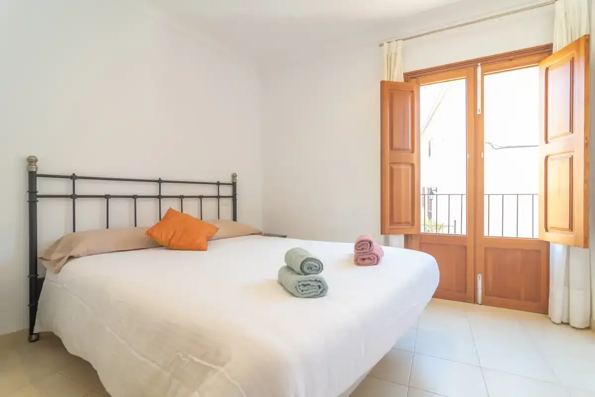 A bedroom with a neatly made bed and an open wooden window.
