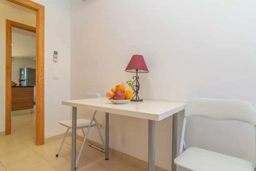 A dining area with a table, chairs, fruit, and a lamp.