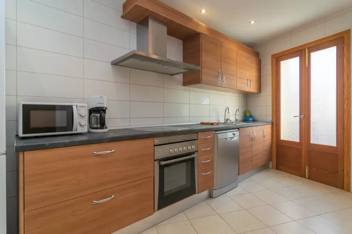 A modern kitchen with wooden cabinets, built-in appliances, and a tiled floor.