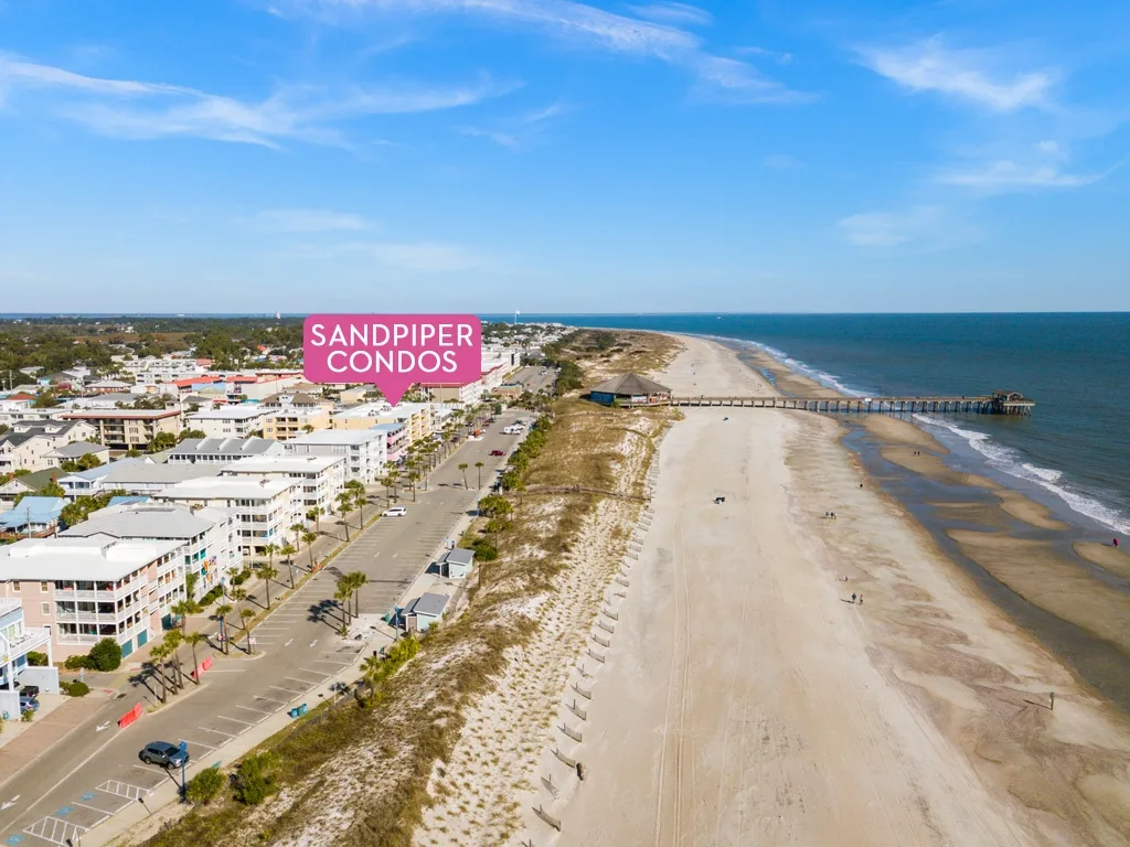 Aerial view of a sandy beach, ocean, and nearby coastal buildings.
