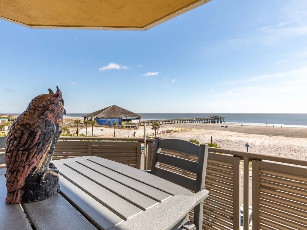 Una mesa y asientos en un patio miran hacia una playa de arena y el agua.
