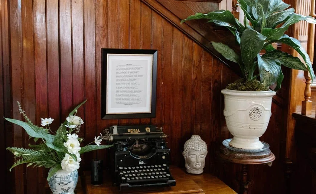 Antique typewriter, statue head, and decorative vases beside dark wooden staircase paneling