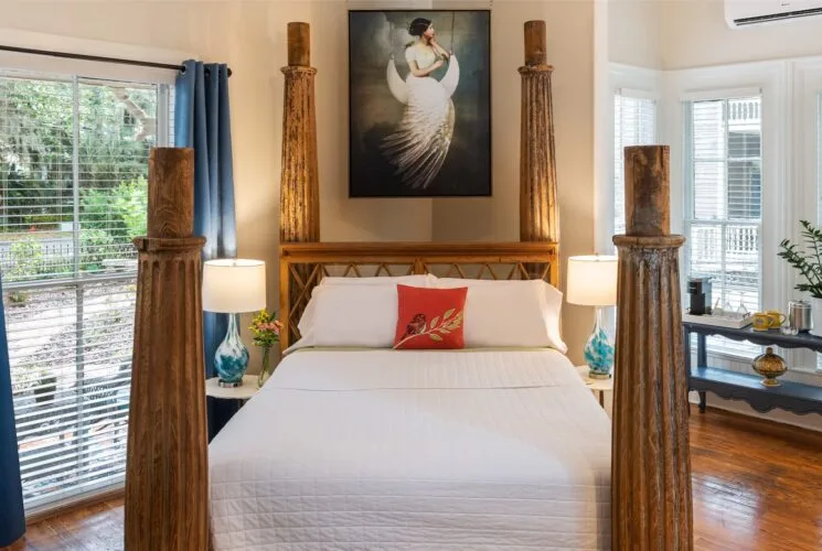 Bedroom with cream walls, hardwood flooring, large wooden bed, white bedding, and windows