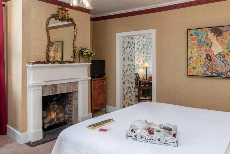 Bedroom with wallpaper, white bedding, fireplace, and ornate mirror