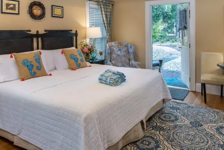 Bedroom with cream walls, hardwood flooring, custom headboard, white bedding, and sitting area