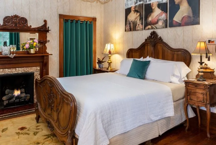Bedroom with wallpaper, hardwood flooring, wooden bed, white bedding, and fireplace
