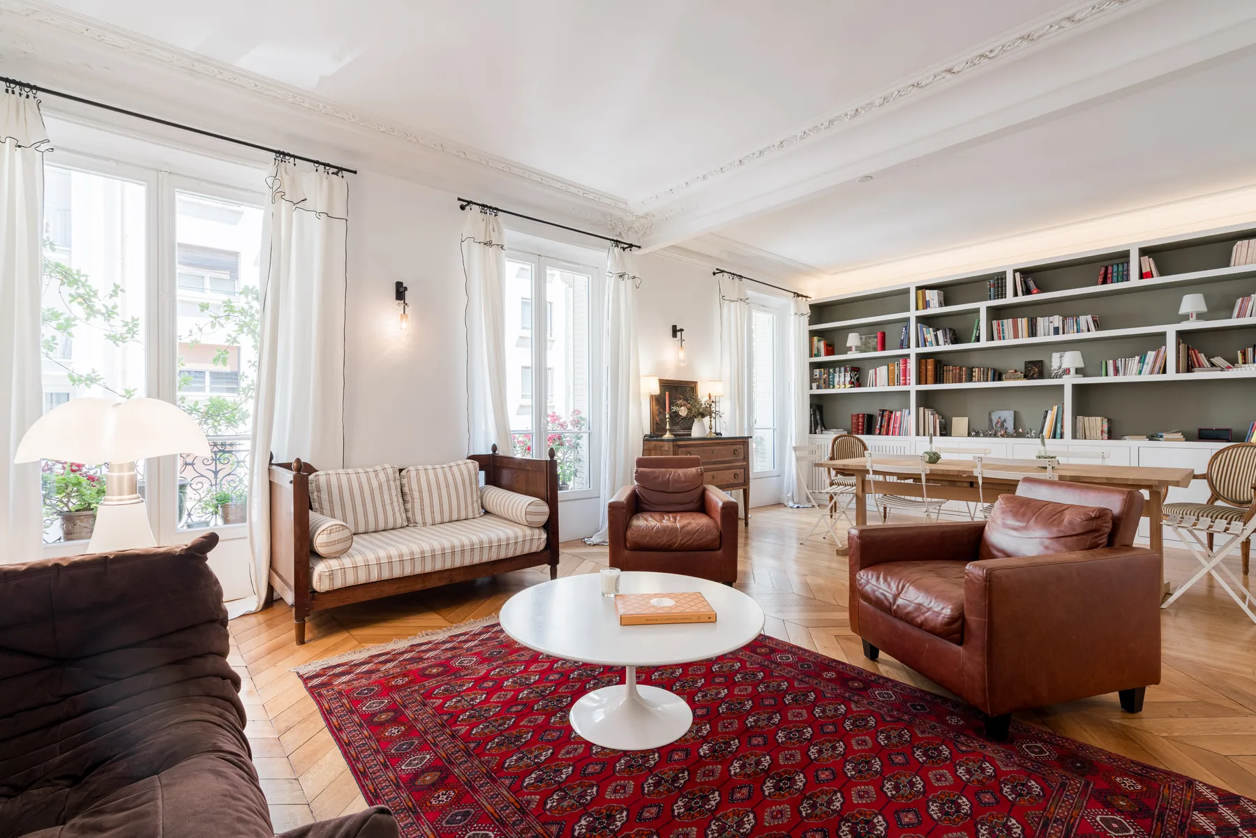 A bright living room with a book-lined wall and seating around a red rug.