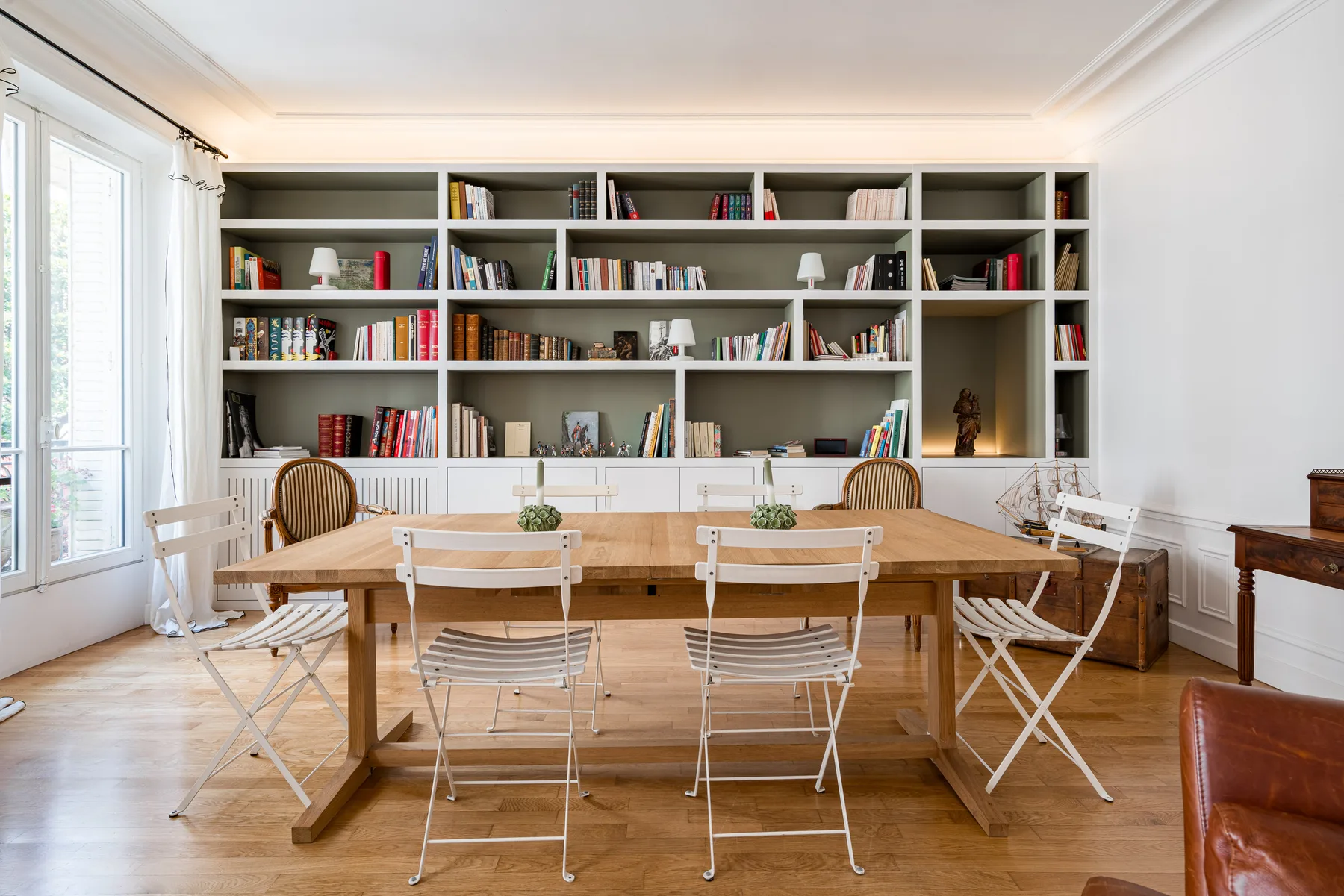 A bright dining area with a wooden table and built-in bookshelves along the wall.