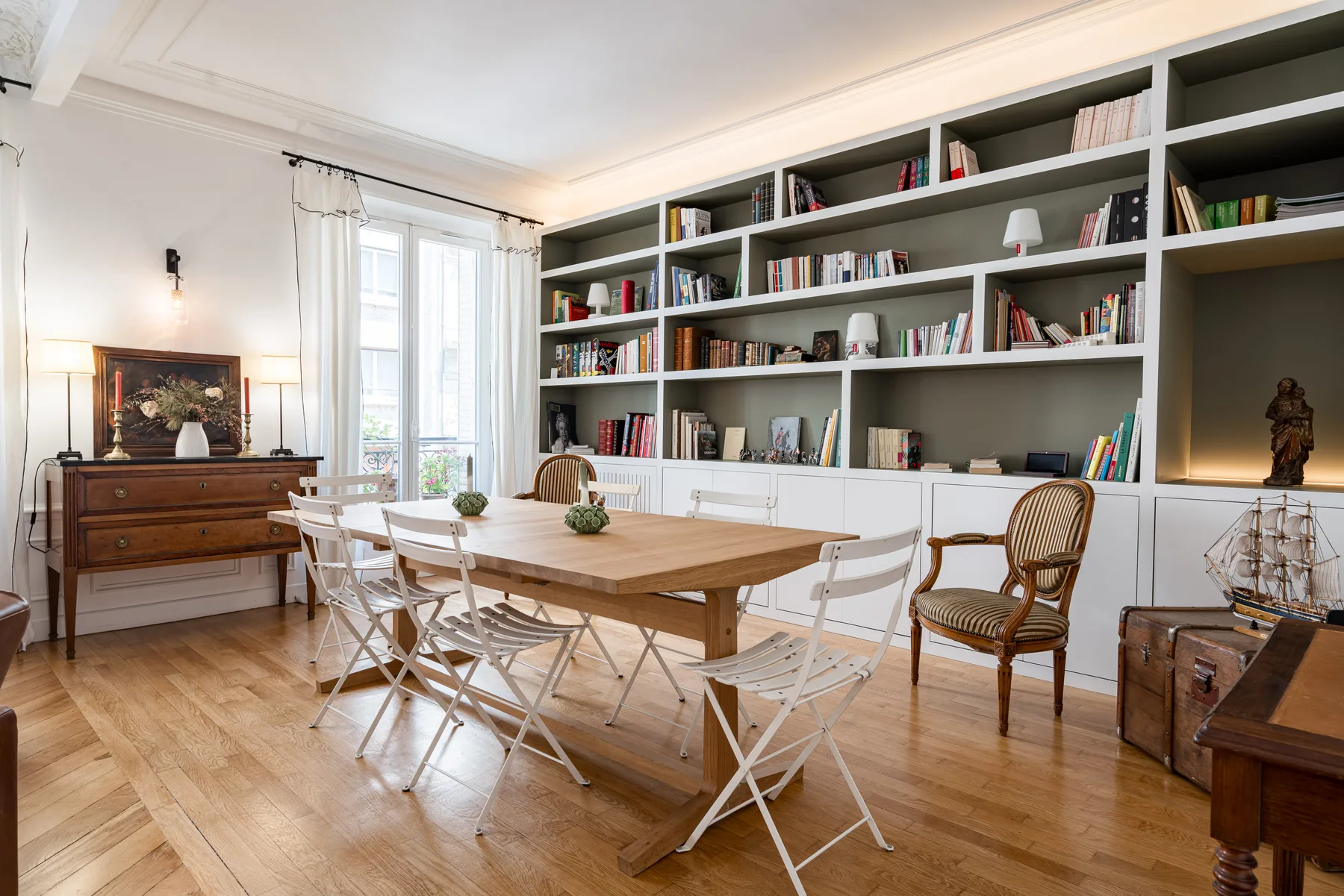 A dining area with a long wooden table and built-in bookshelves along the wall.