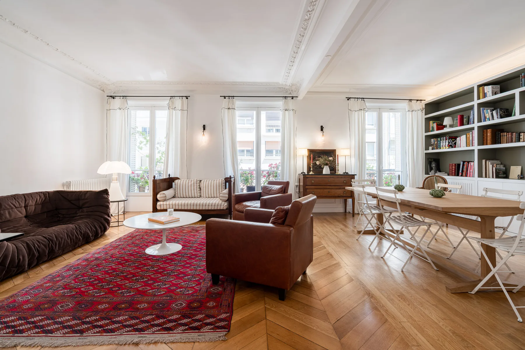 A bright living room with seating around a patterned rug and a dining table.