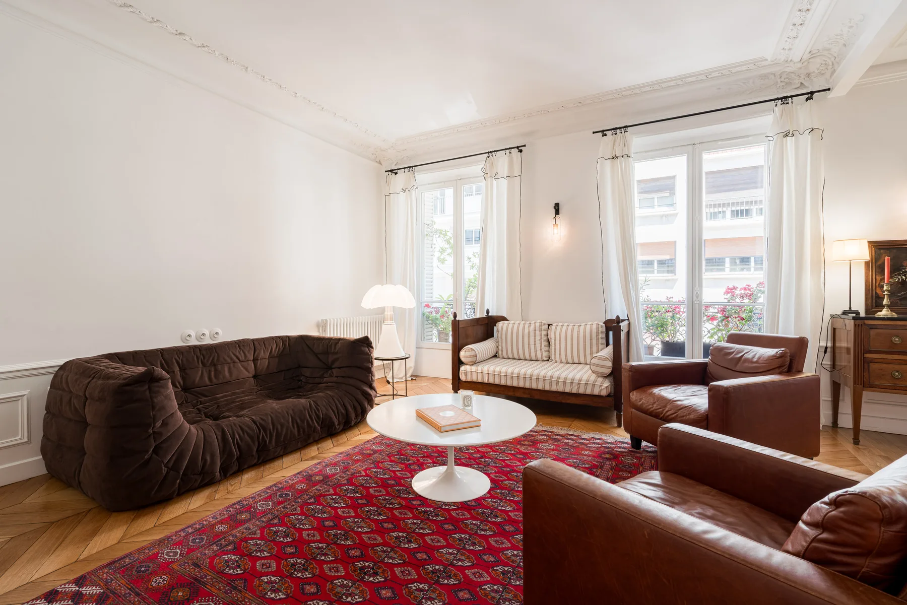 A bright living room with seating around a white coffee table on a patterned rug.
