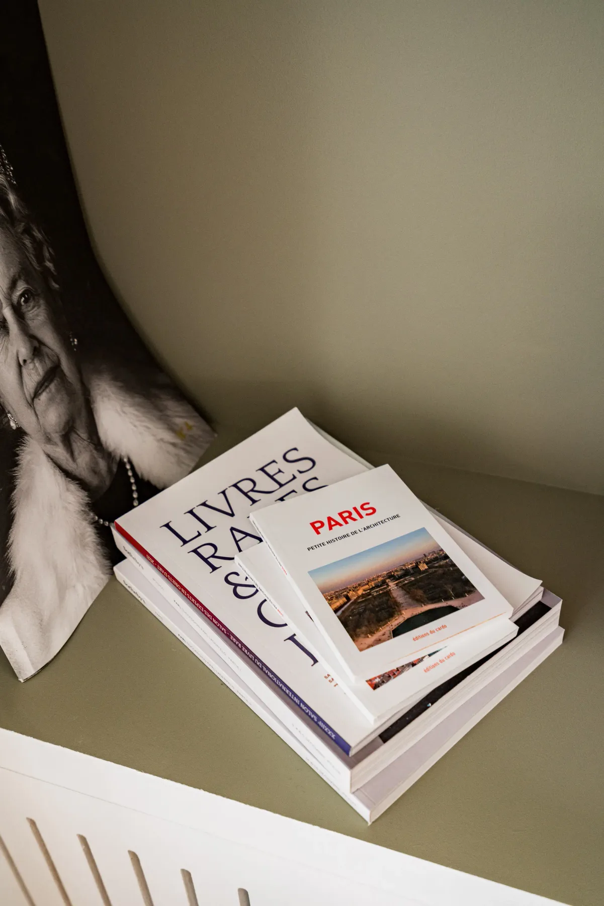 Books rest on a shelf beside a black-and-white portrait.