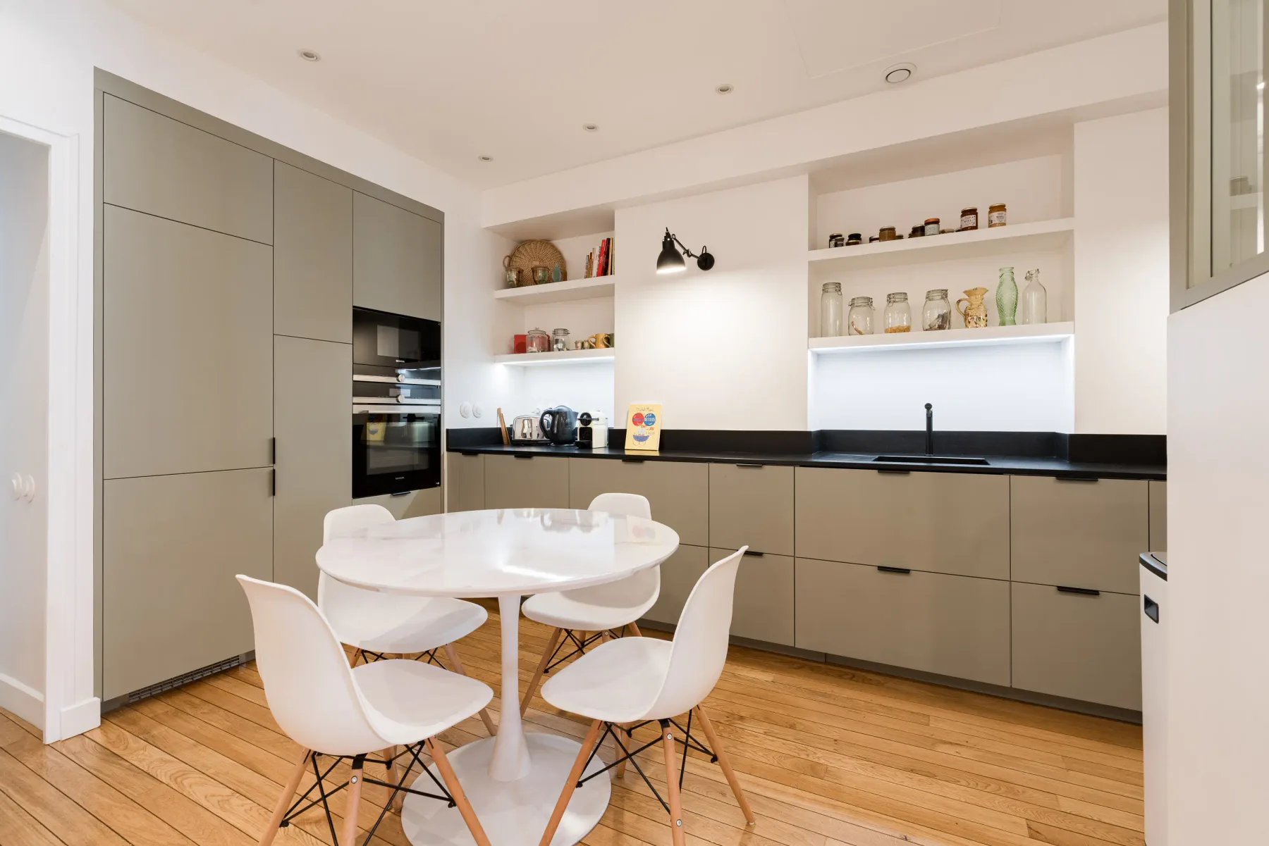 A modern kitchen with gray cabinets, open shelving, and a round dining table.