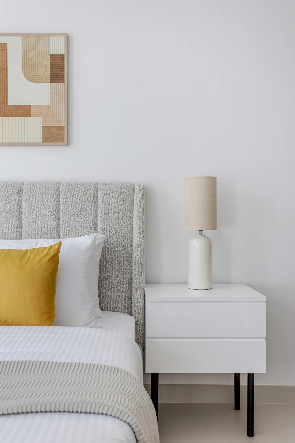 A bedroom with a neatly made bed and a white bedside table.