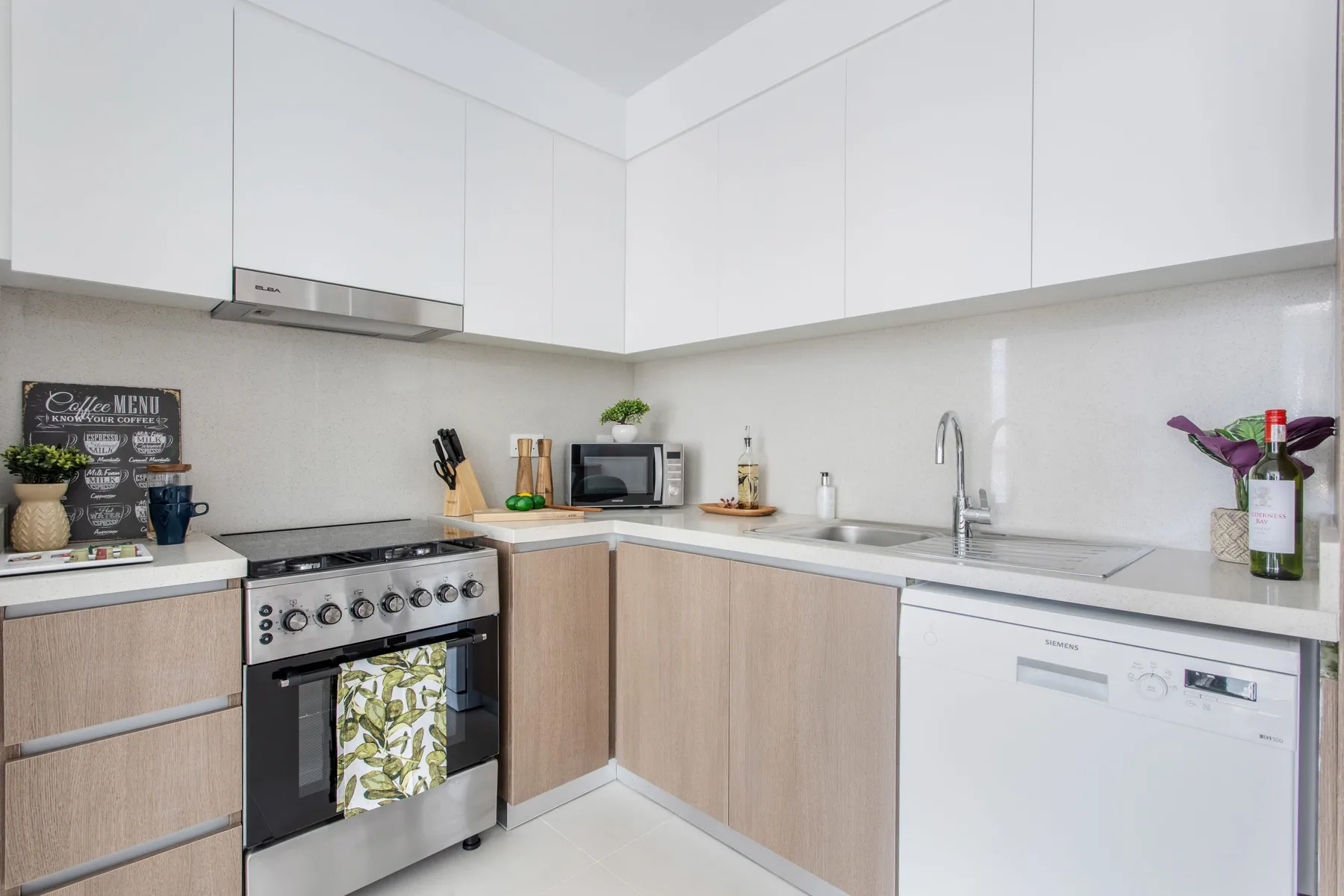 A bright kitchen with light cabinets, a stove, microwave, and sink.