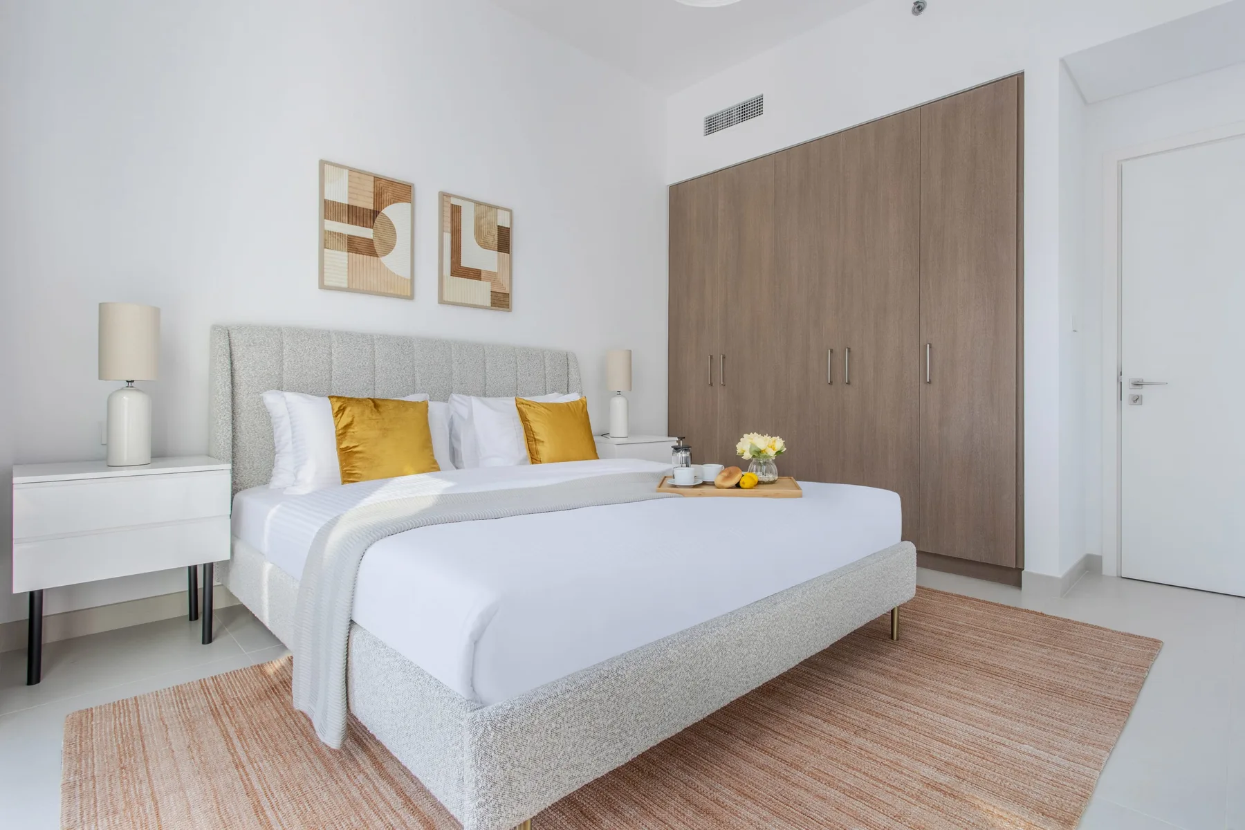 A bright bedroom with a neatly made bed, white bedding, and wooden wardrobes.