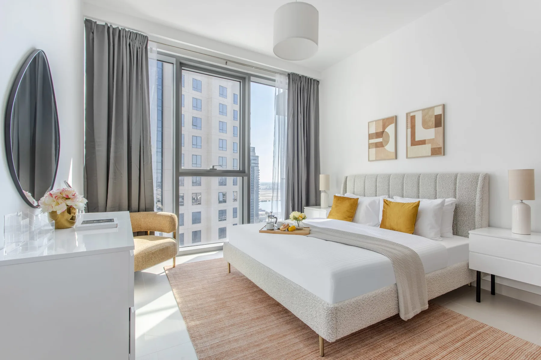 A bright bedroom with a neatly made bed, bedside tables, and a large window.