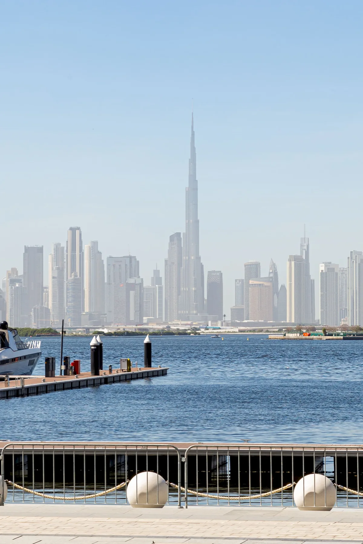 A waterfront promenade overlooks the water and a distant city skyline.