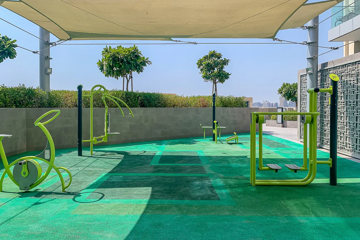 An outdoor fitness area with exercise equipment beneath a shade canopy.