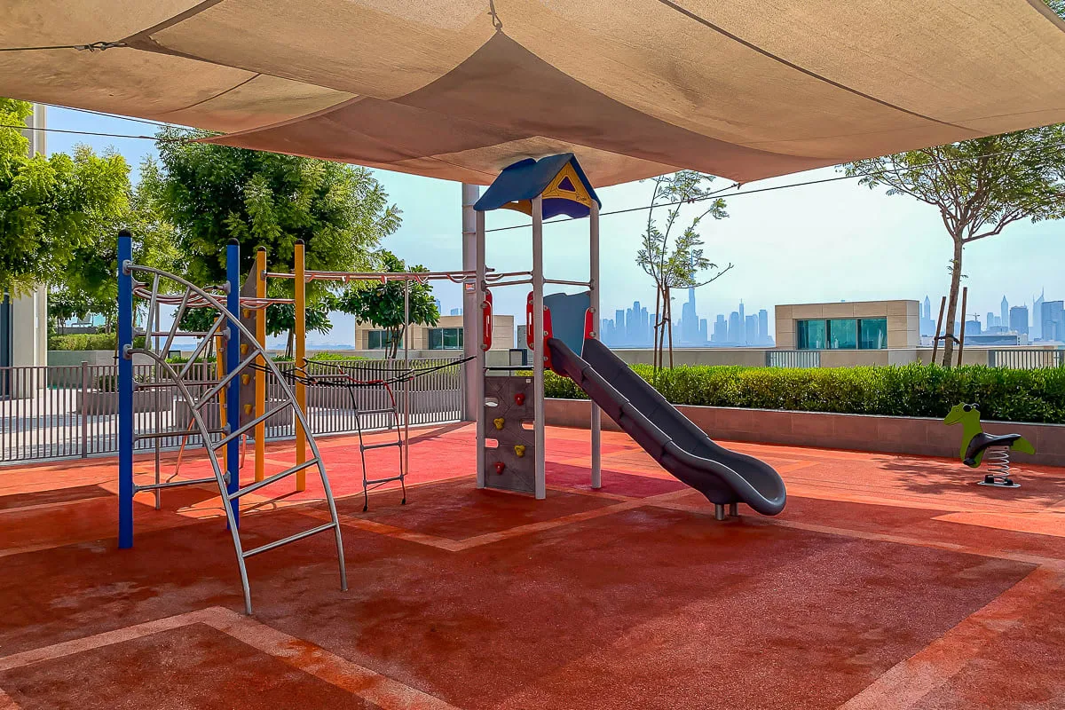 A shaded outdoor playground with climbing equipment and a slide.