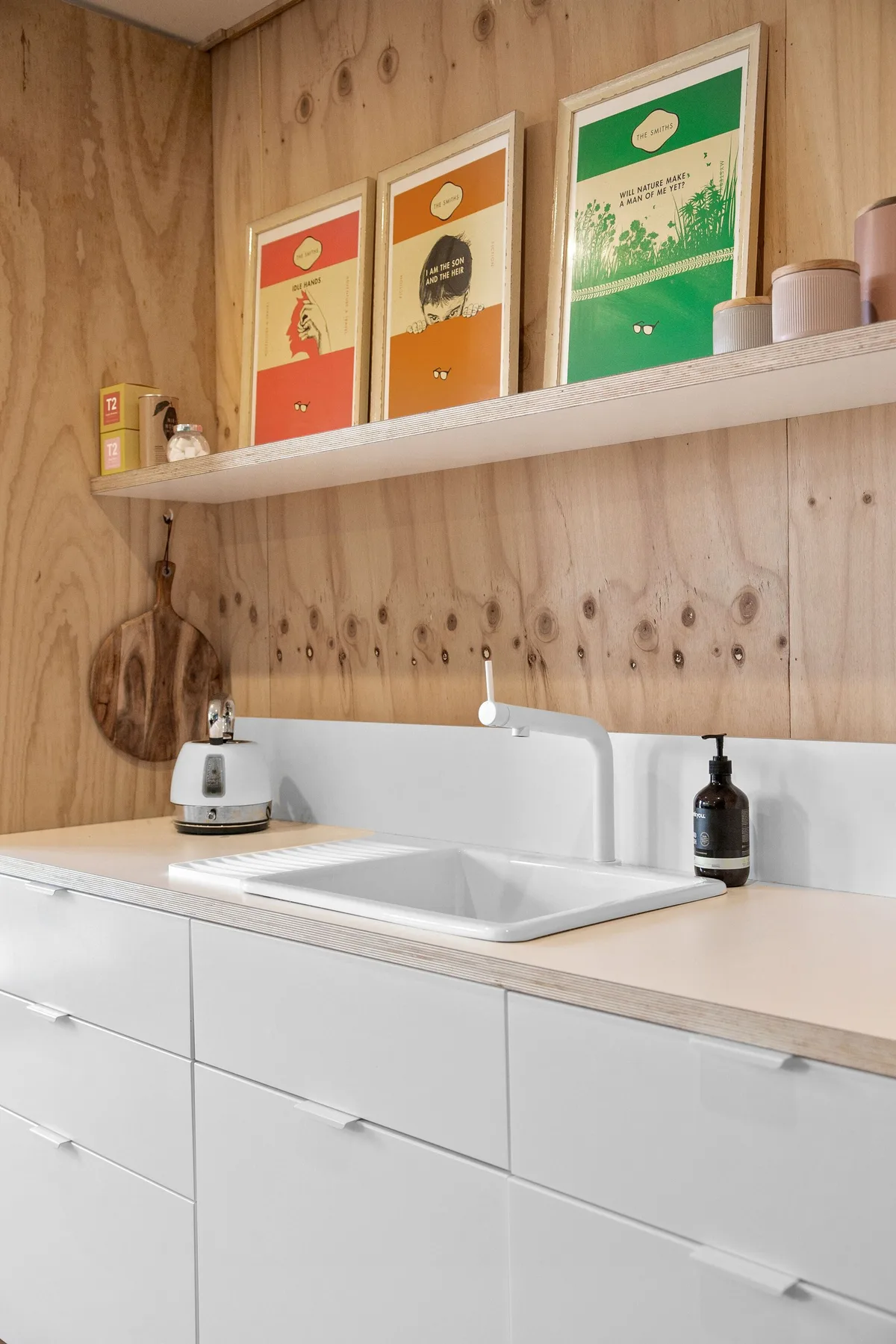 Una cocina compacta con fregadero y gabinetes blancos junto a una pared de madera.