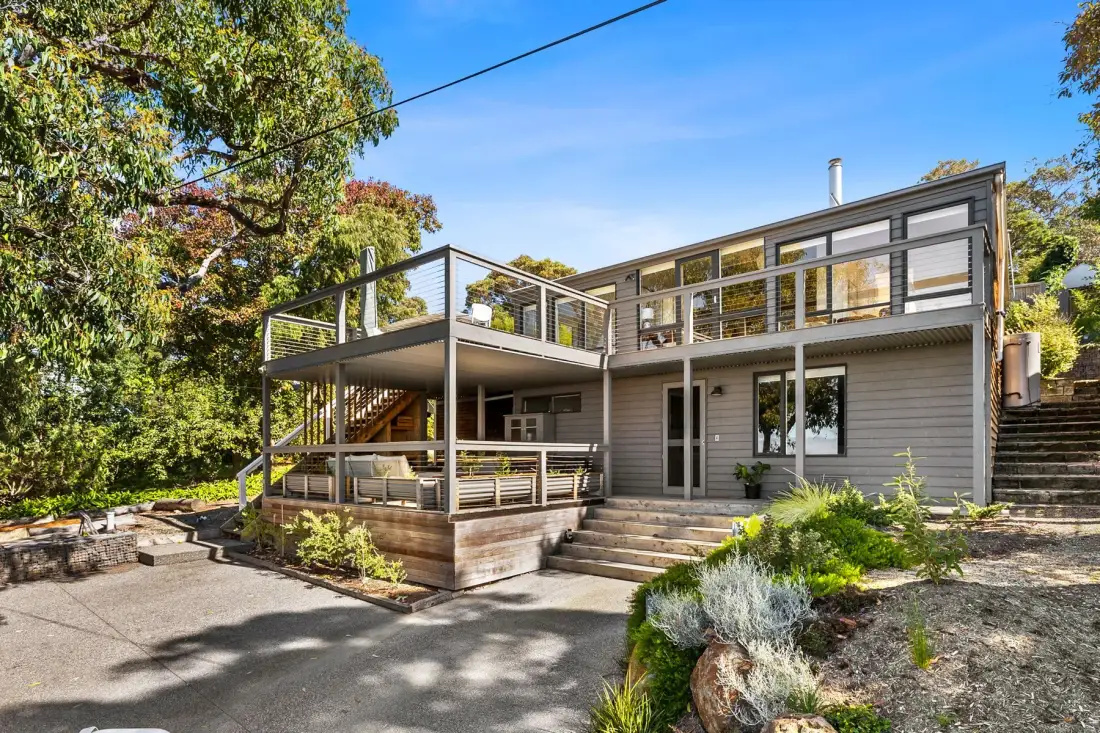 A modern two-story house with broad wooden decks sits among trees.