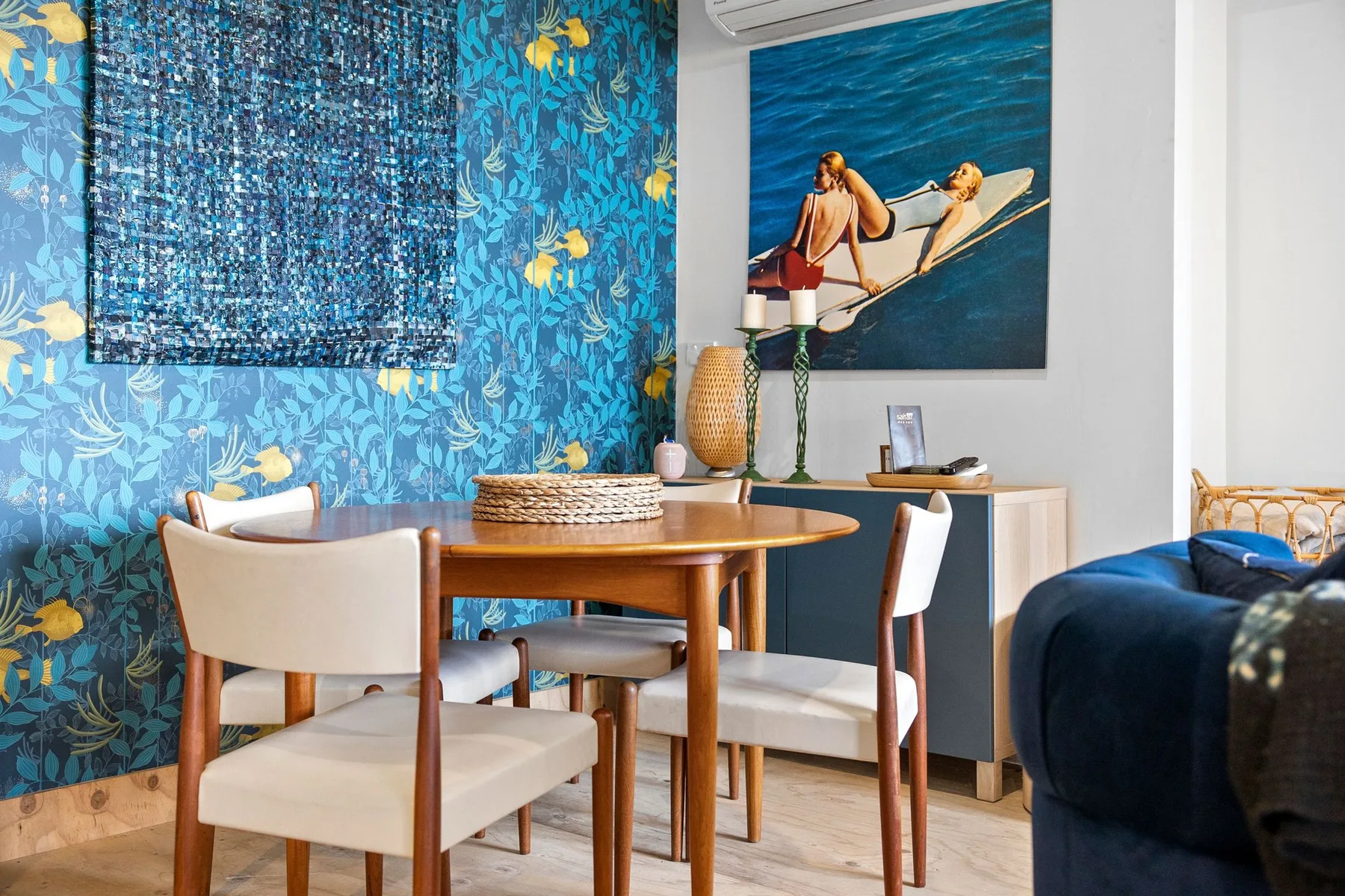 Un comedor con una mesa redonda de madera junto a una pared azul estampada.