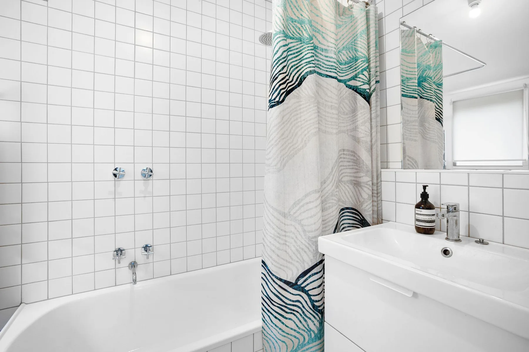 Un baño alicatado con bañera, cortina de ducha estampada y lavabo.