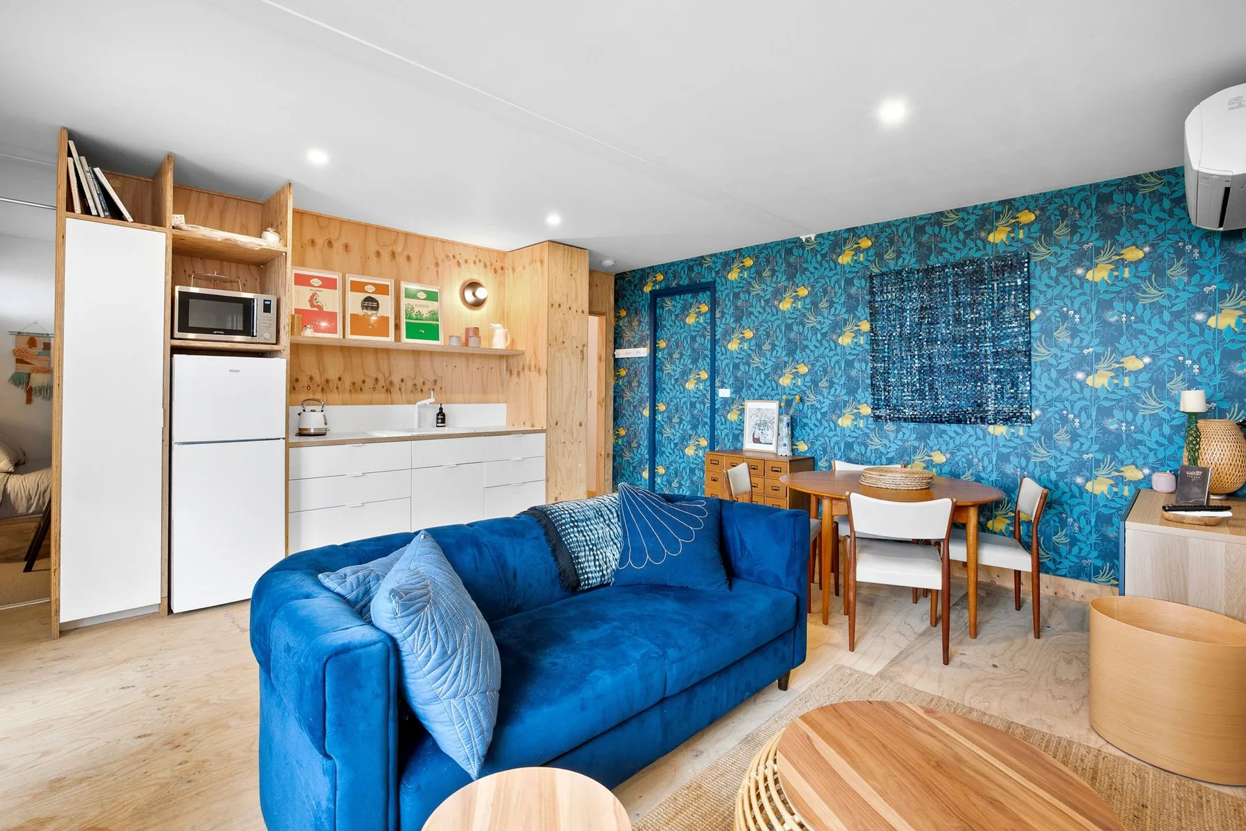 Una sala azul con asientos, una mesa de comedor y una cocina compacta.