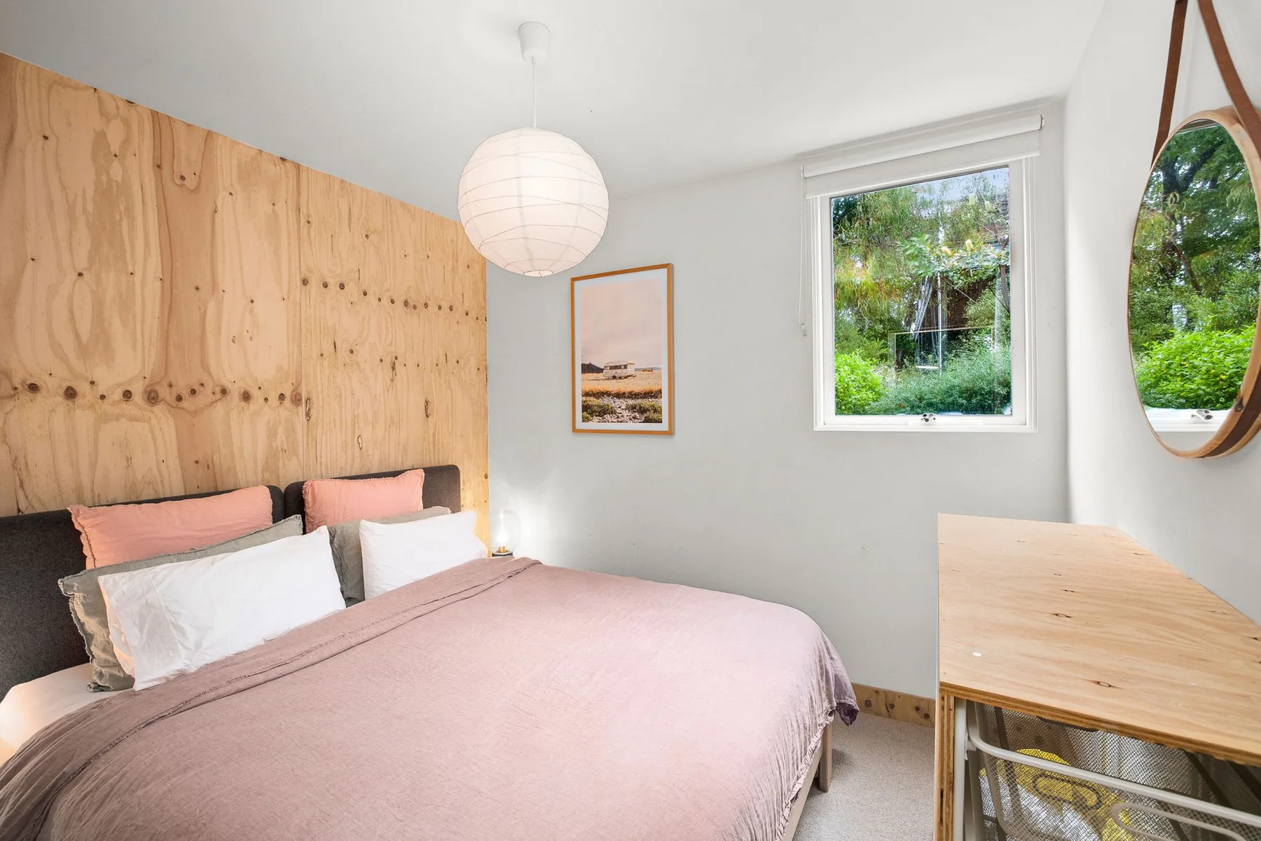 Dormitorio con cama, ropa de cama rosa pálido y una pared revestida de madera.
