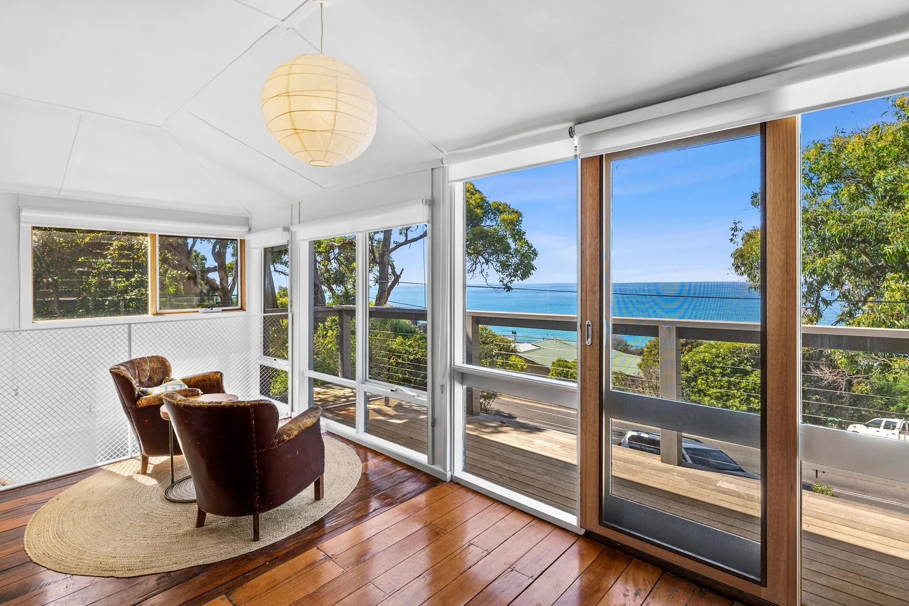 A bright sunroom with large windows overlooking the ocean and a seating area.