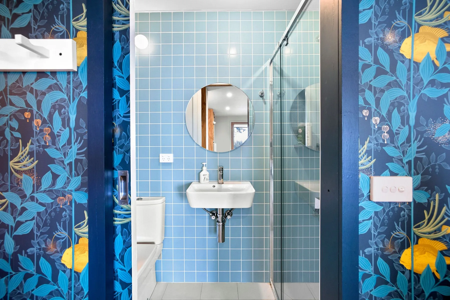 Un baño con paredes de azulejos azules y una ducha de vidrio.