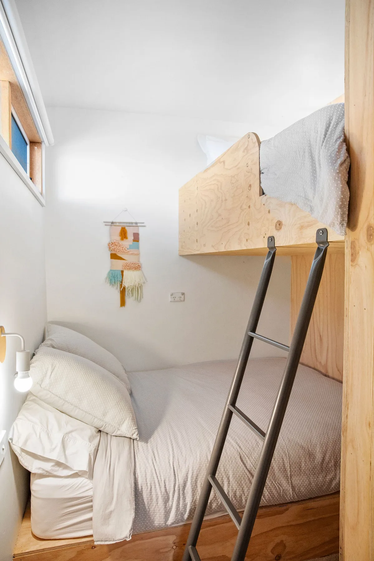 Un dormitorio compacto con una cama elevada y una escalera junto a una cama inferior.