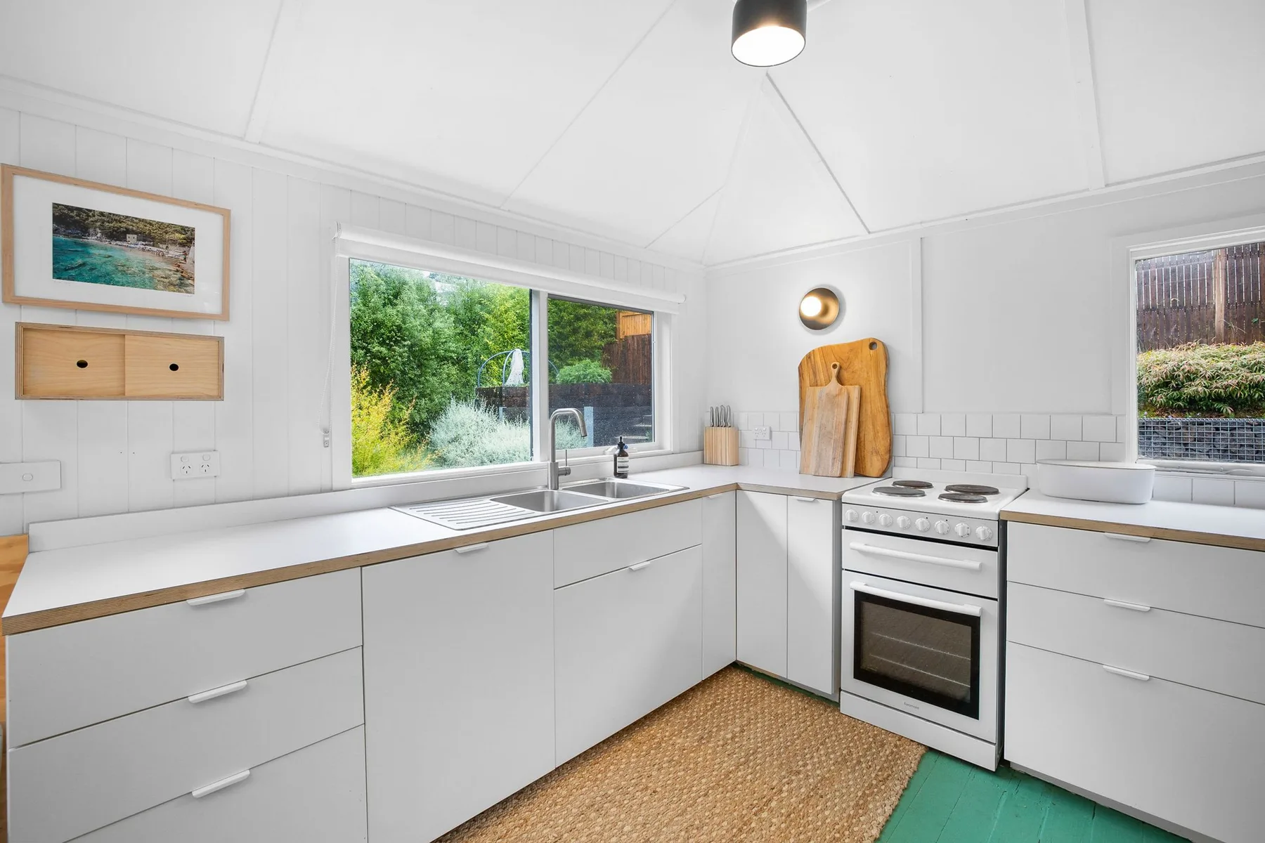 Una cocina luminosa con gabinetes blancos y una ventana con vista a la vegetación.