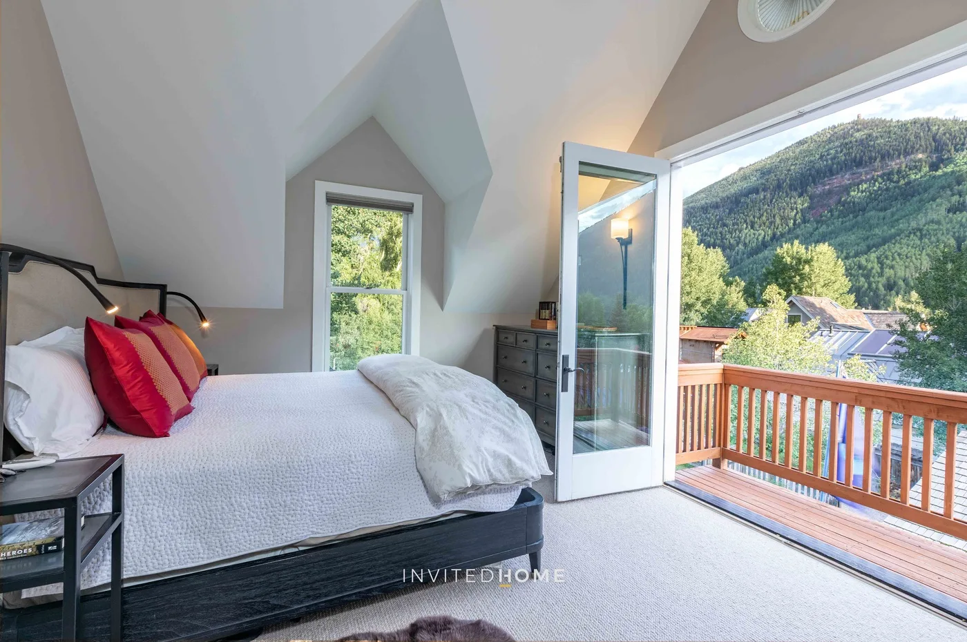 Un dormitorio con una cama junto a una puerta abierta al balcón, con vista a una ladera verde.