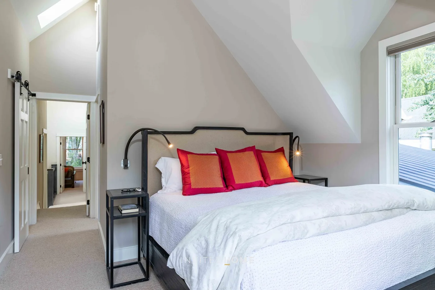 Un dormitorio abuhardillado y luminoso tiene una cama con cojines coloridos junto a una ventana.