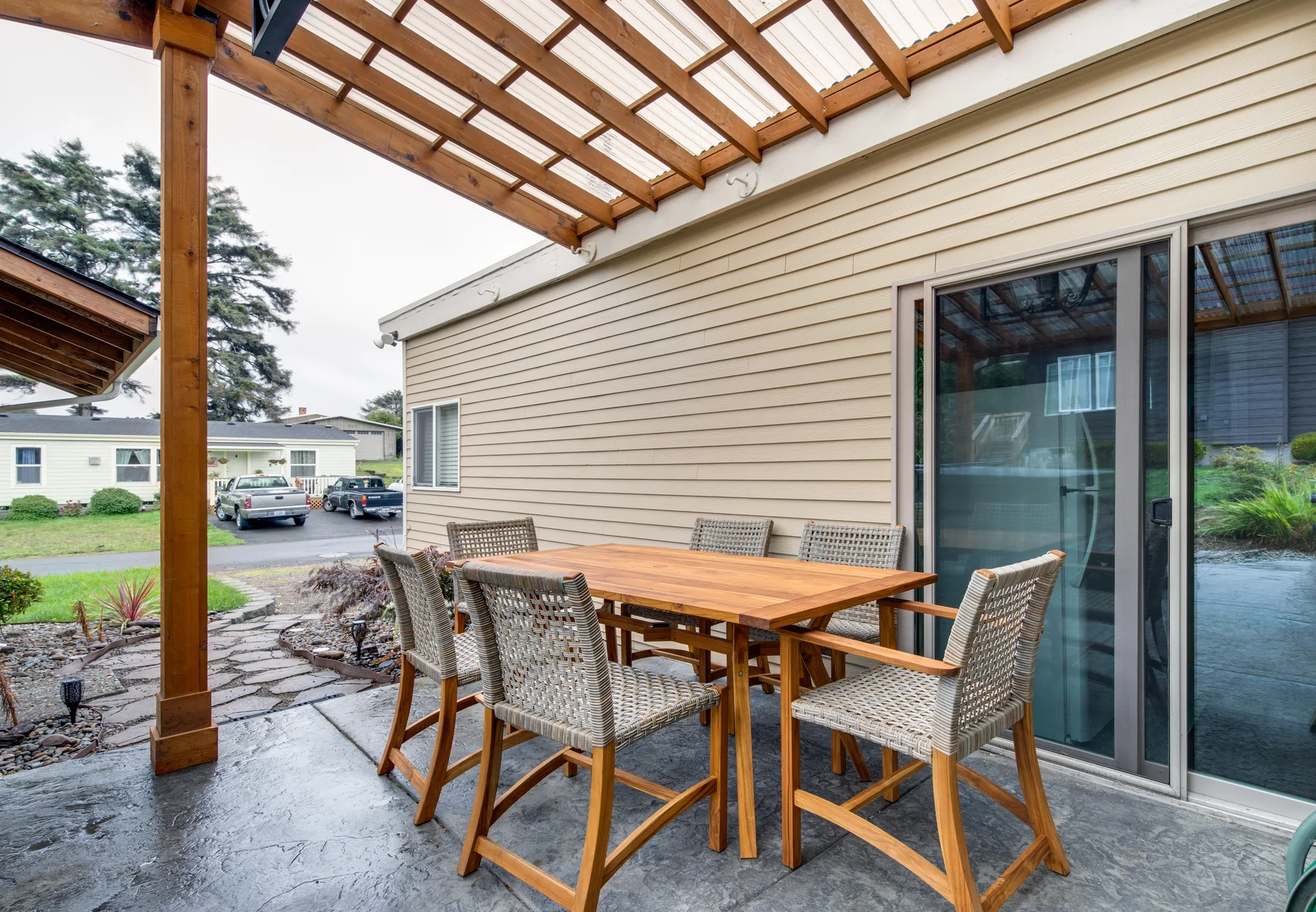 A covered outdoor patio with a wooden dining table and woven chairs beside sliding glass doors.