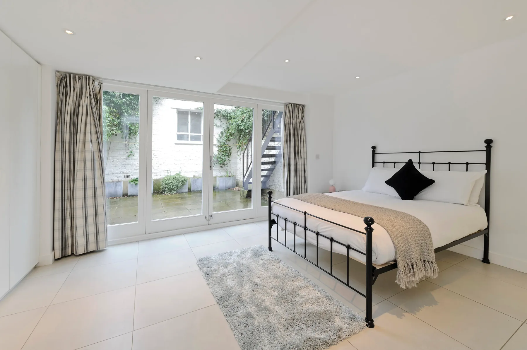 A bright bedroom with a black metal bed beside full-height windows.