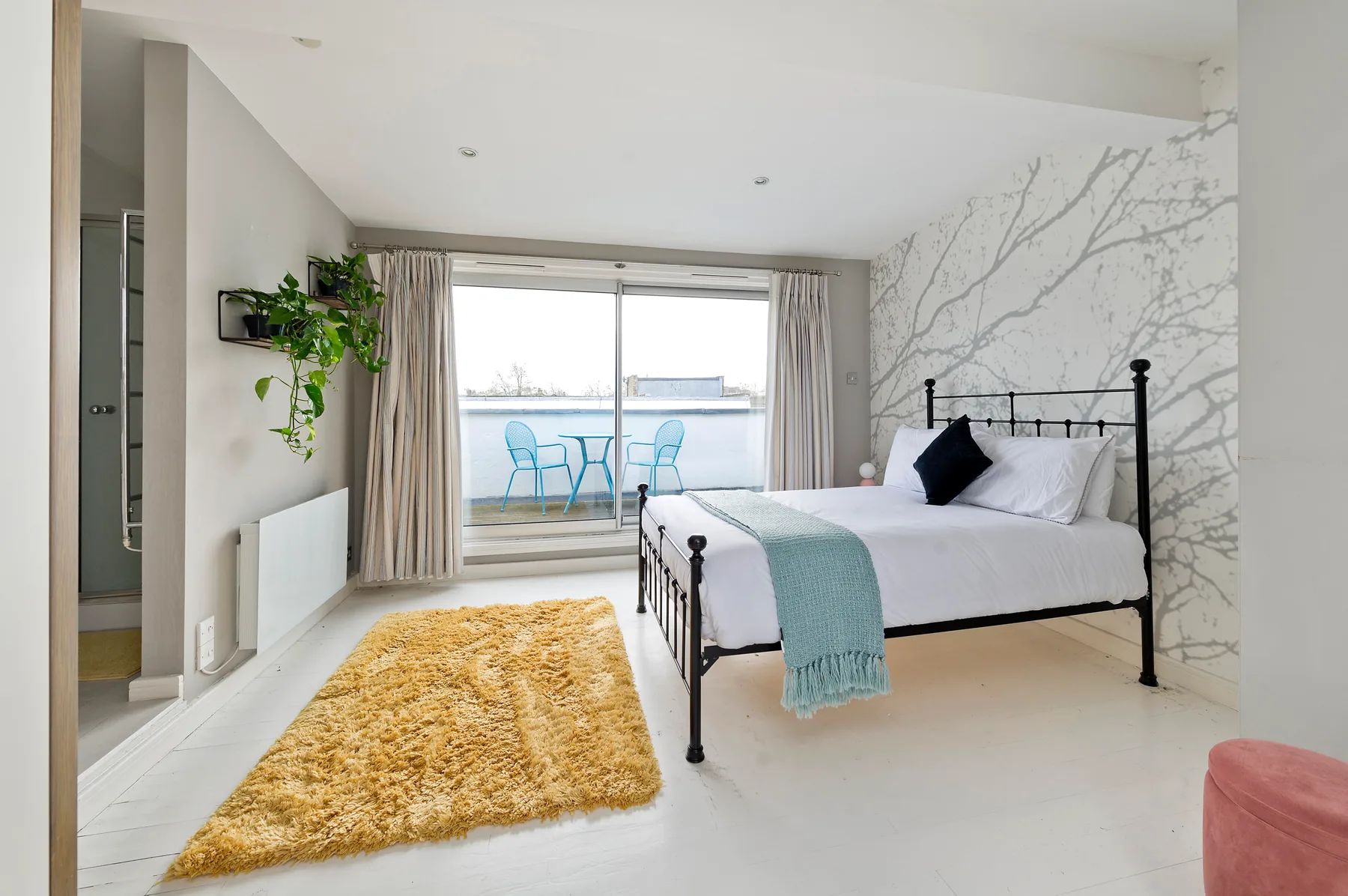 A bright bedroom with a black bed frame and sliding glass doors opening onto a balcony.