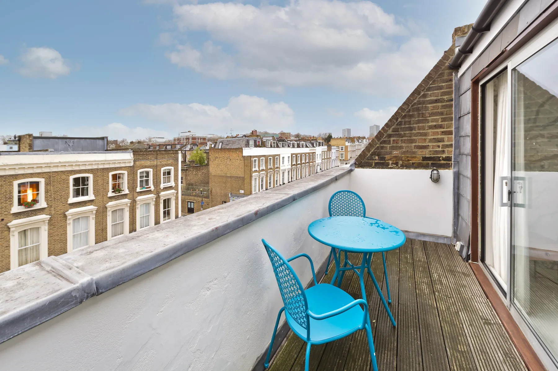 A rooftop terrace with bright blue seating overlooks a row of brick buildings.