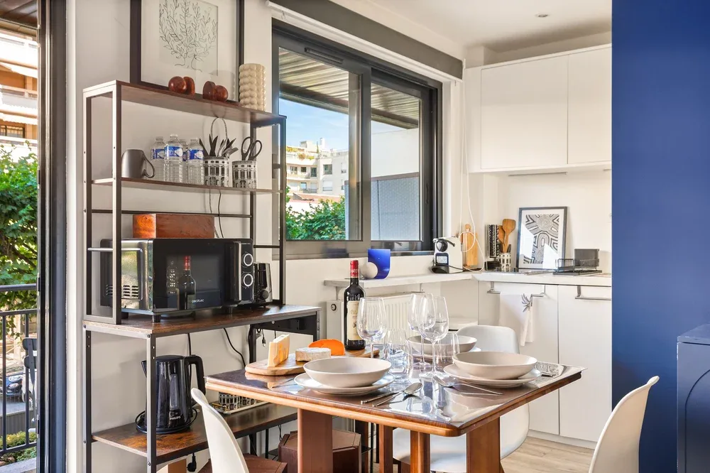 Comedor con la mesa puesta junto a una ventana amplia y armarios de cocina.
