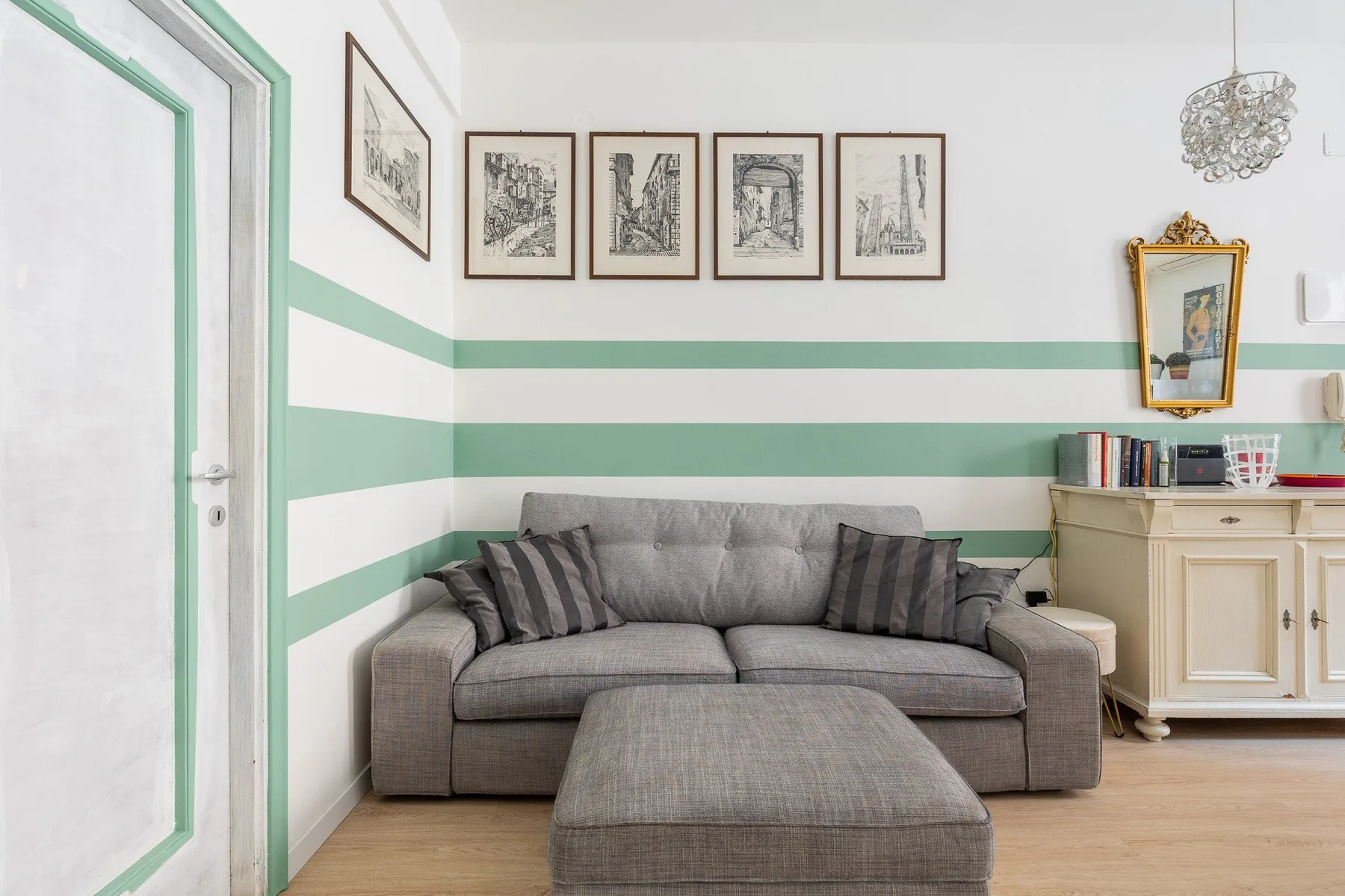 Una sala de estar con un sofá gris bajo cuadros enmarcados y franjas verdes en la pared.
