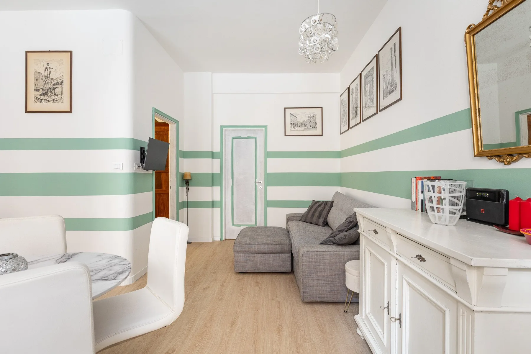 Una sala de estar luminosa con asientos, un aparador blanco y franjas verdes en las paredes.