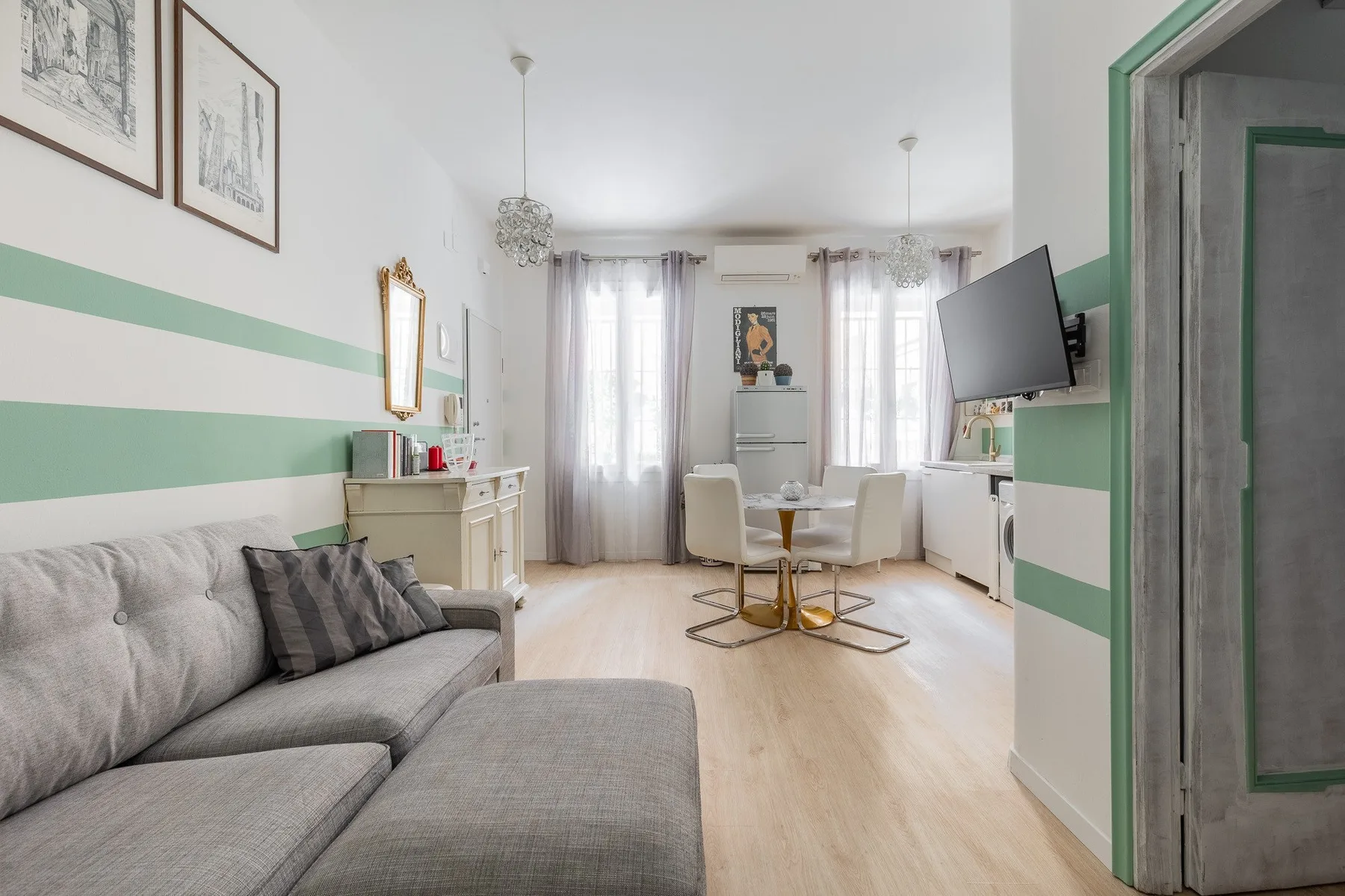 Una sala luminosa con asientos grises, una mesa de comedor y ventanas altas.