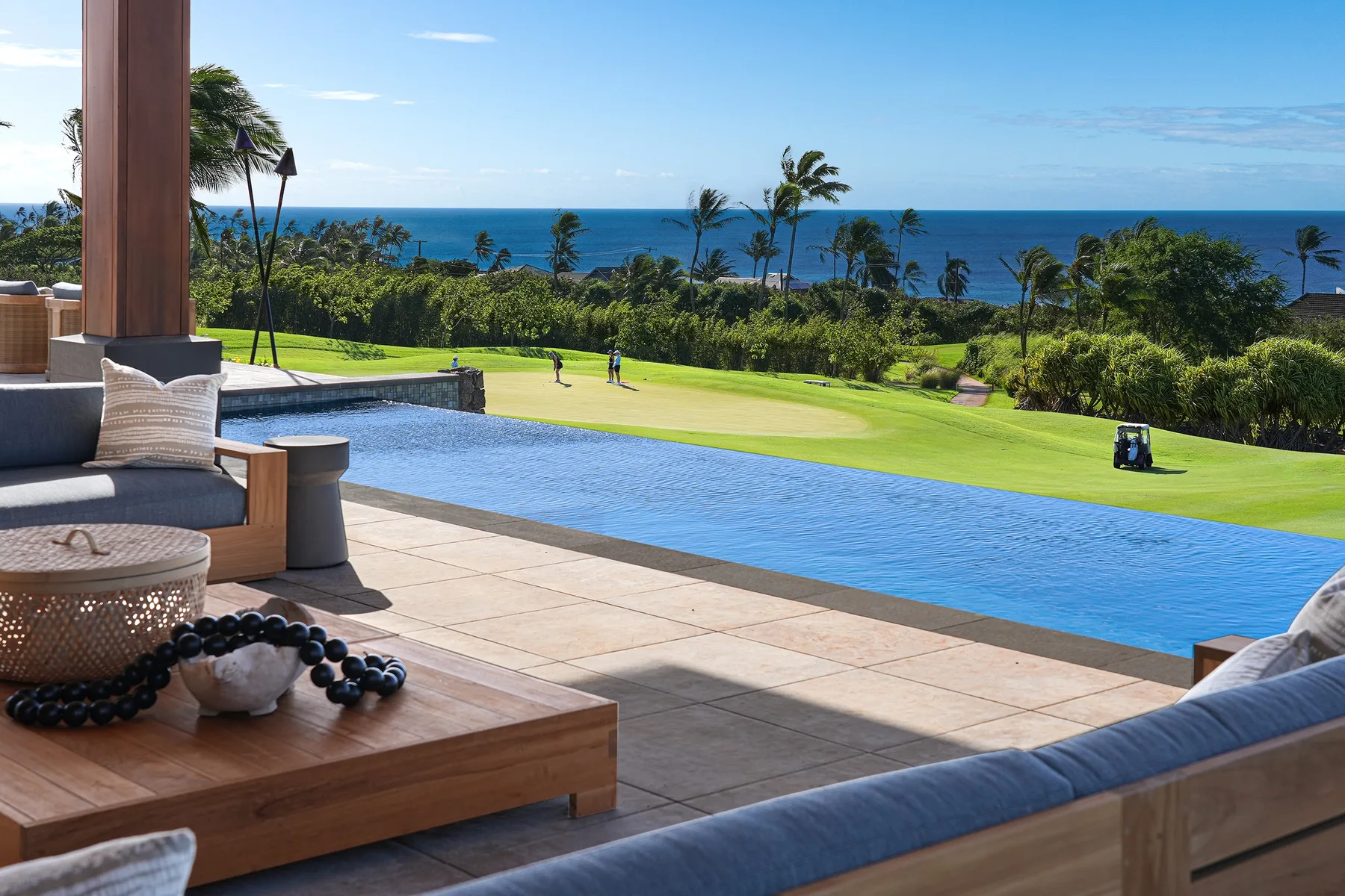An outdoor poolside terrace overlooks a green lawn and the ocean.
