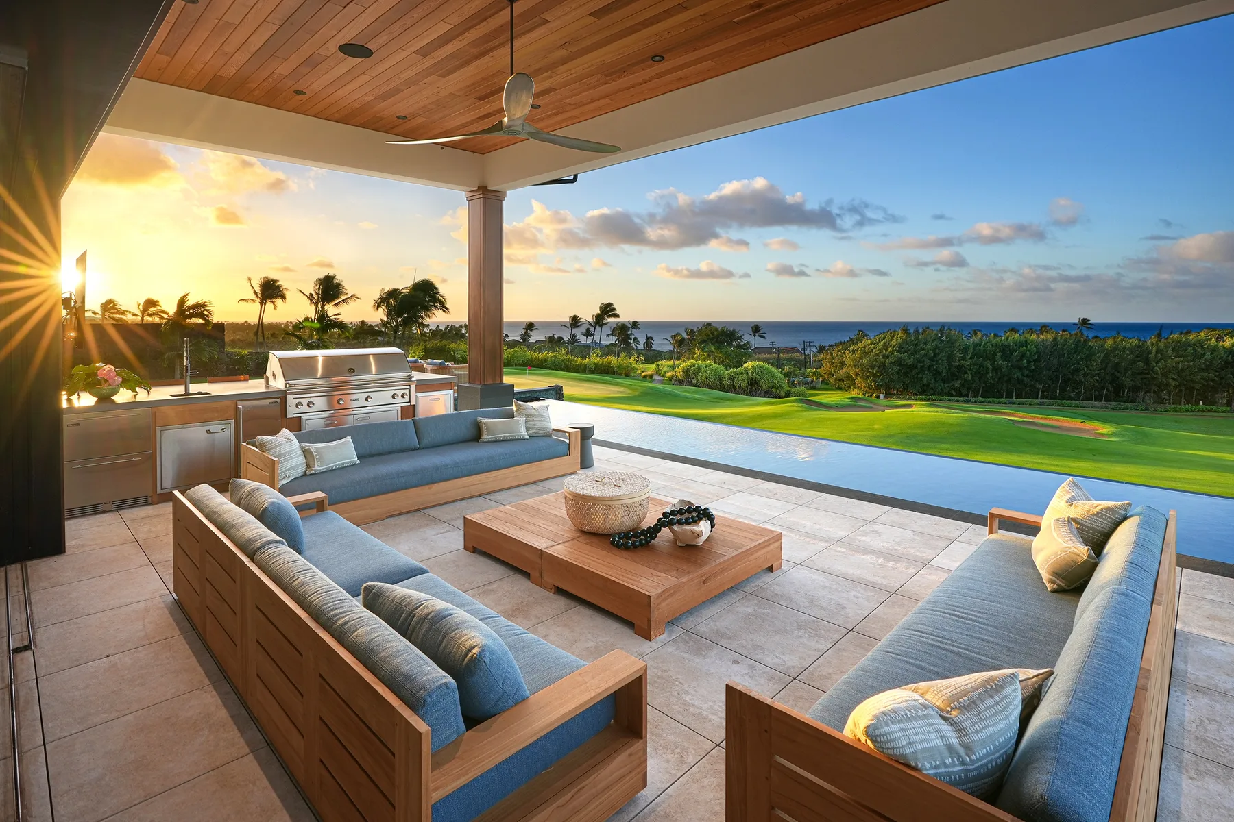 A covered outdoor lounge with cushioned seating overlooks a pool and ocean.