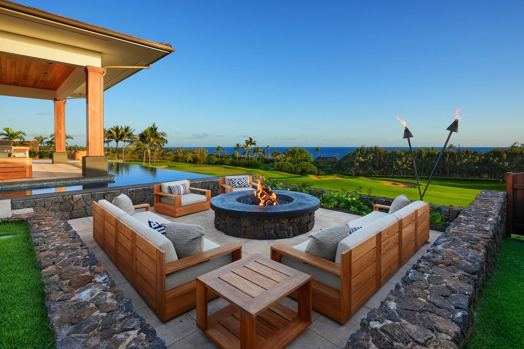 An outdoor lounge with seating around a fire pit overlooks the ocean.