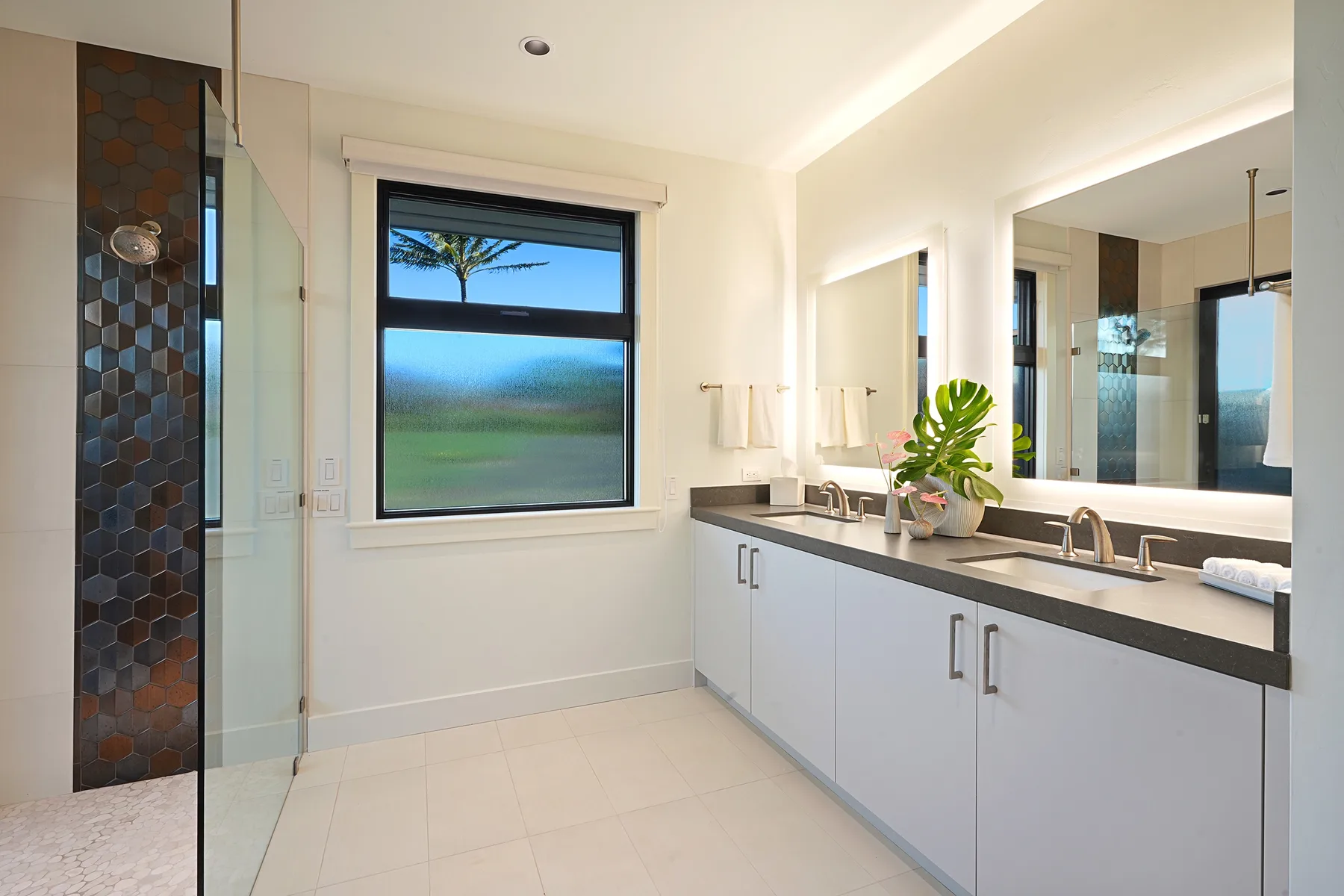 A bright bathroom with a glass shower, a large window, and a long vanity.
